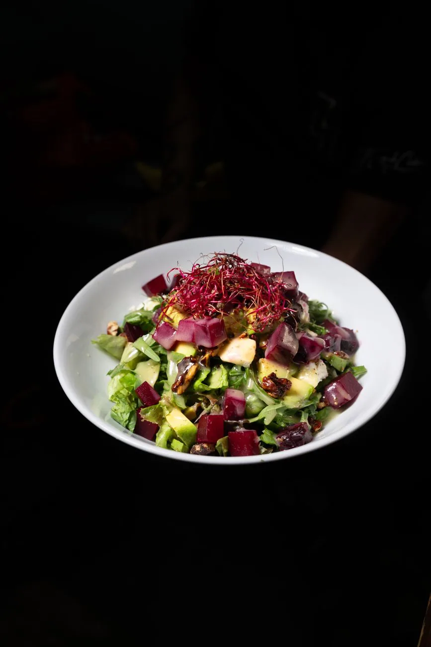 Ensalada de betarraga, palta, hojas verdes y nueces servida en un bowl blanco